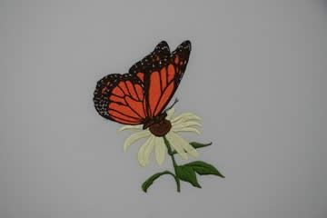 Monarch butterfly with orange and black wings, perched on a white flower with green leaves.