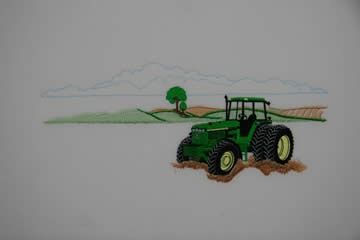 Green tractor plowing a field, with hills, tree, and mountain in the background.