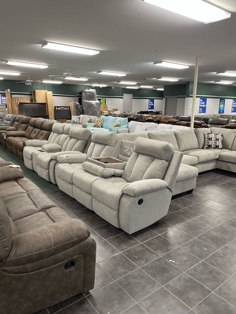 A furniture store displays multiple sofas and recliners in various colors, with overhead fluorescent lighting.