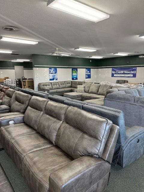 Inside a furniture store, various gray couches are displayed under bright lights.