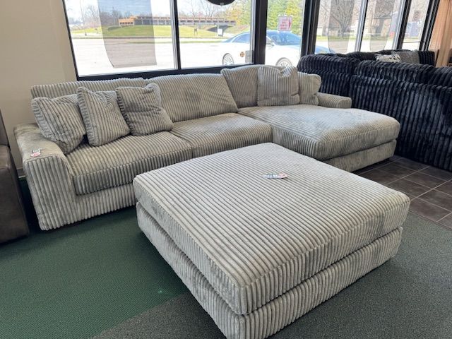 Gray corduroy sectional sofa with matching ottoman in a store.