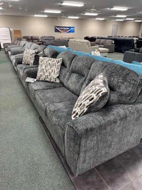 Gray sofa with patterned pillows in a furniture store, with other sofas in the background.
