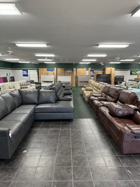 A furniture store interior. Rows of sofas in brown, beige, and gray. Overhead lighting.