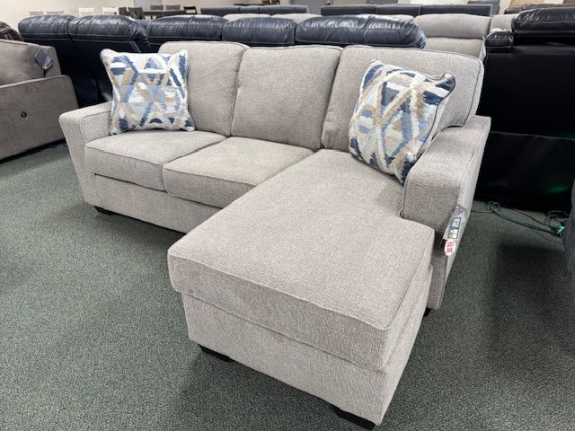 Light gray sectional sofa with blue patterned accent pillows in a showroom.