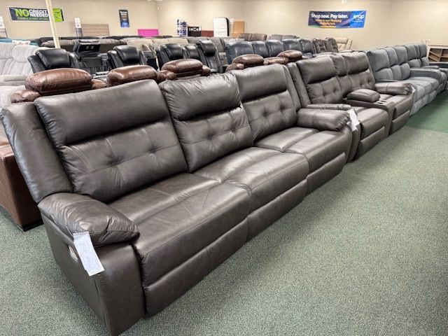 Dark brown leather reclining sofas in a showroom, on a green carpet.
