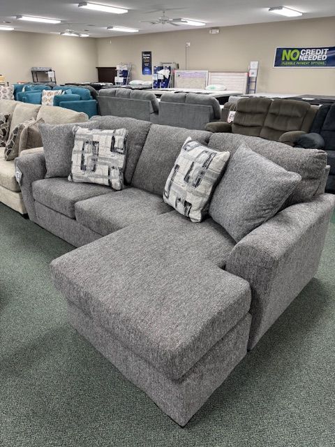 Gray fabric sectional sofa with two patterned throw pillows in a furniture store.