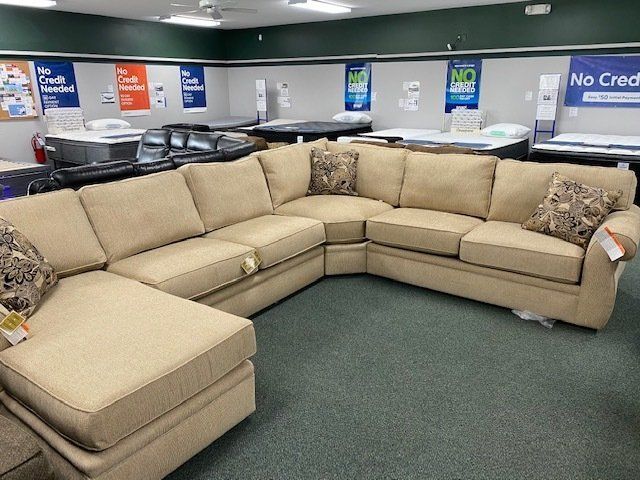Beige sectional sofa in a furniture store, with mattresses in the background.