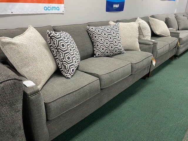 Gray sofa with decorative pillows on green carpet in a showroom.
