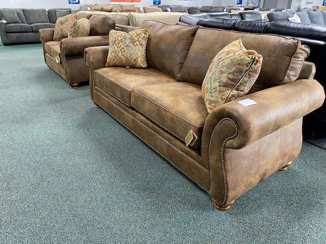 Brown leather sofa with rolled arms and patterned throw pillows in a furniture store.