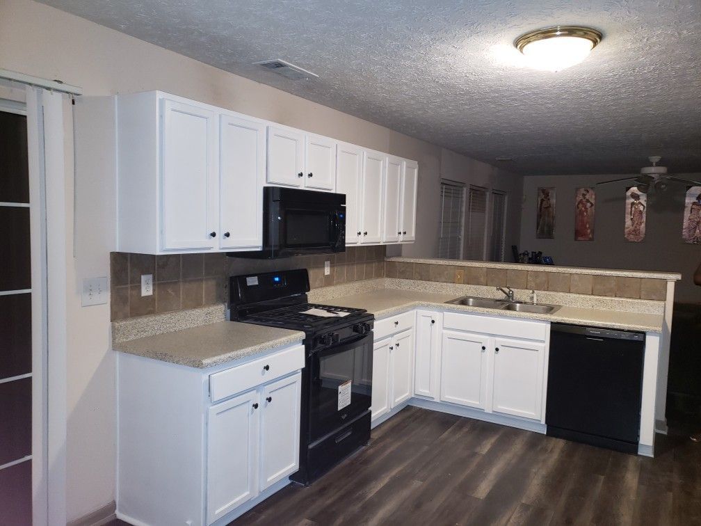 A kitchen with white cabinets , a stove , a microwave , and a dishwasher.