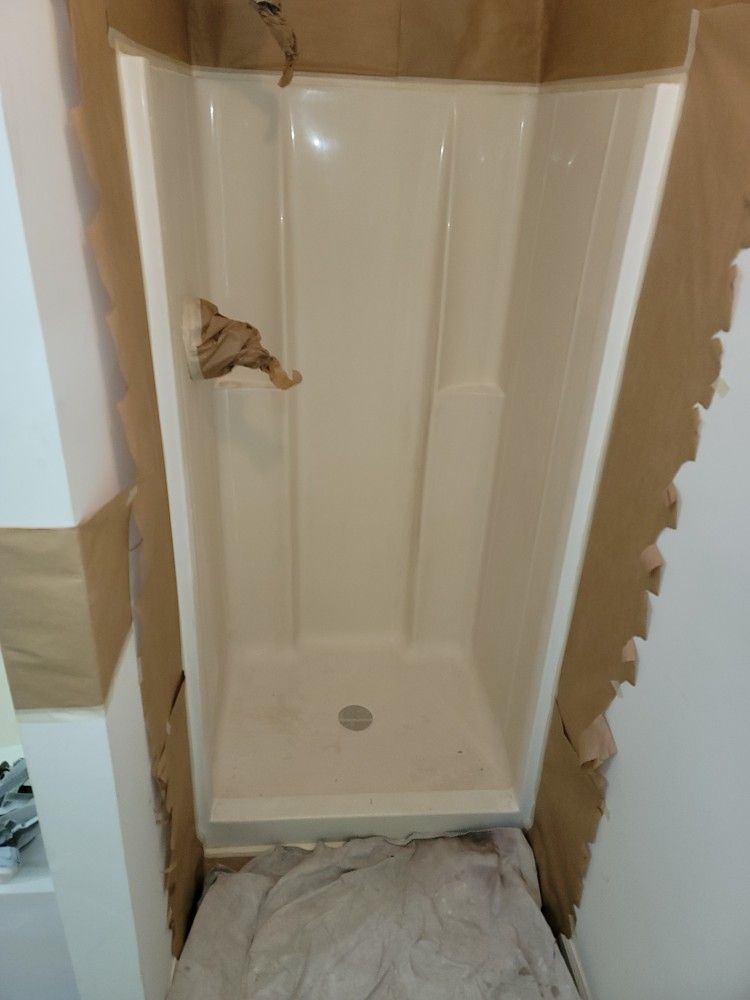 A white shower stall is being installed in a bathroom.