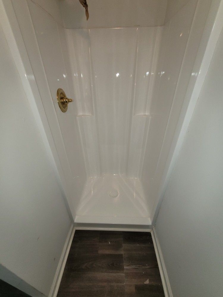 A white shower stall with a wooden floor in a bathroom.