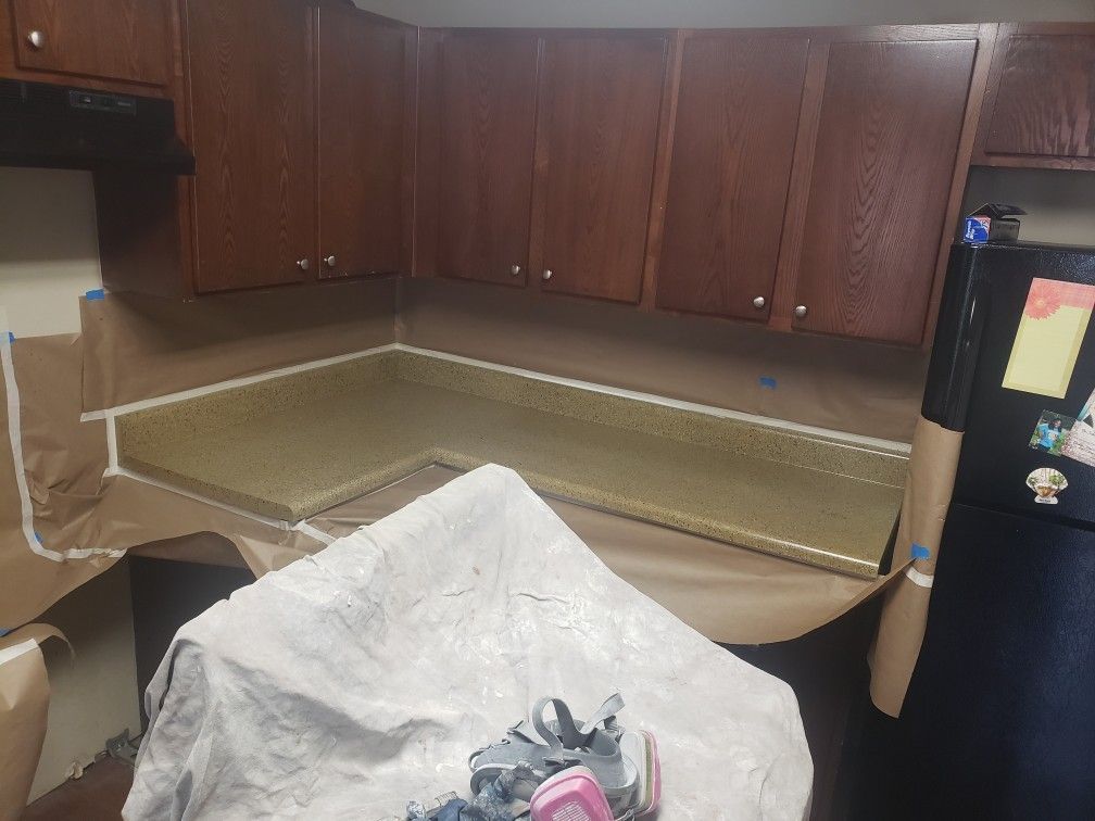 A kitchen with wooden cabinets and a black refrigerator is being painted.