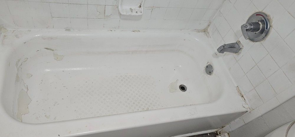 A dirty bathtub in a bathroom next to a toilet.
