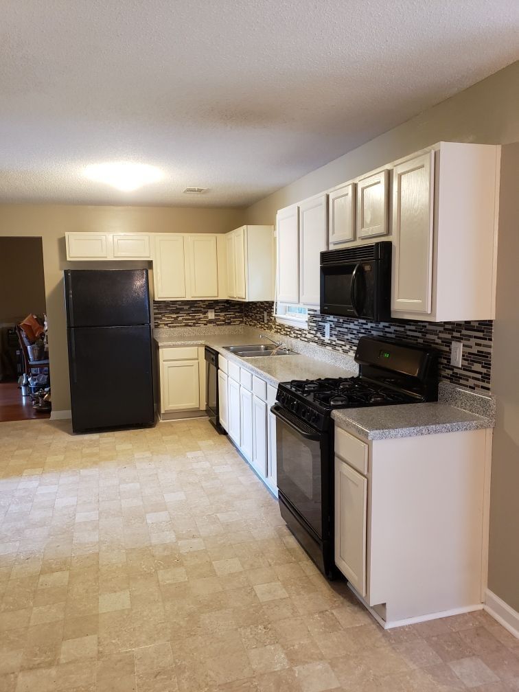 A kitchen with white cabinets , a black refrigerator , a stove , and a microwave.