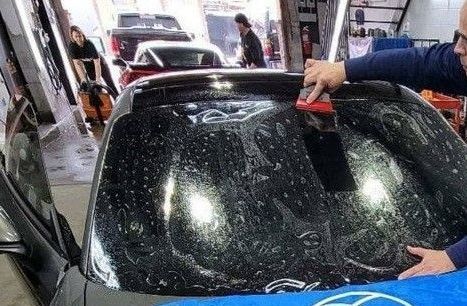 A man is cleaning the windshield of a car in a garage.