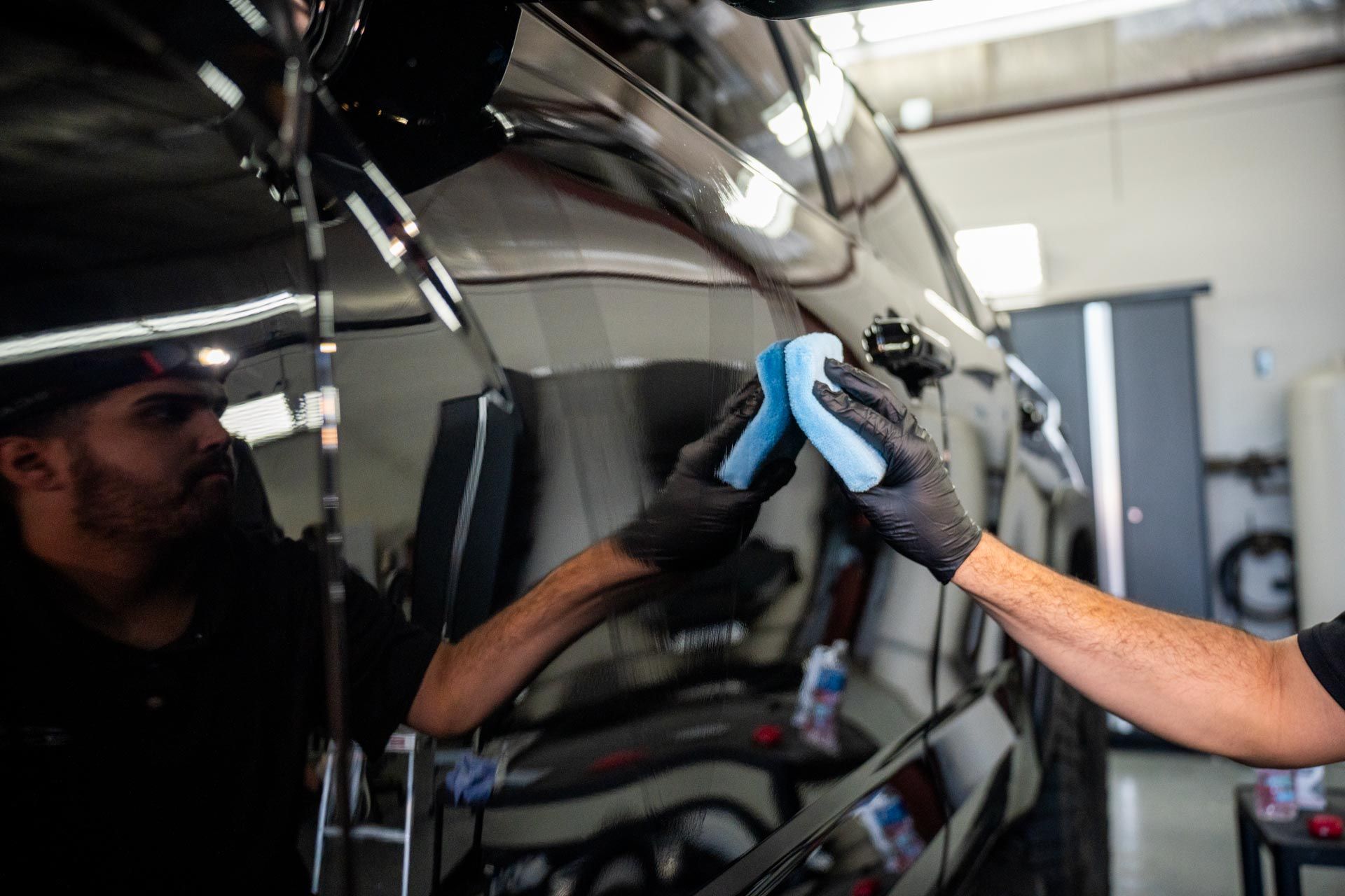 A man is polishing a car with a sponge in a garage.