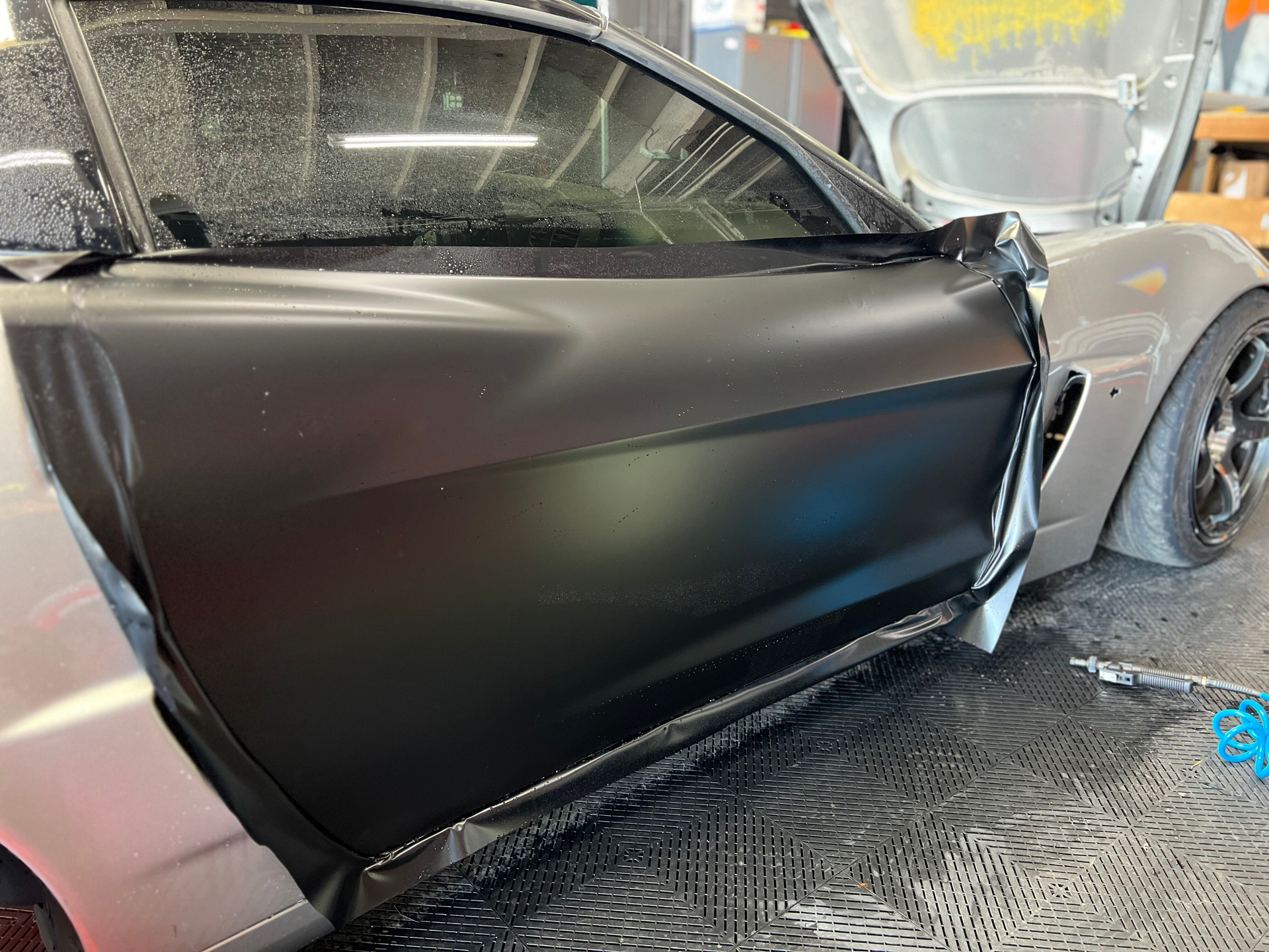 A silver sports car is sitting on a tiled floor with its door open.