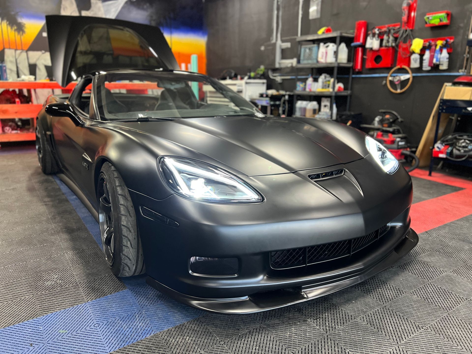 A black sports car is parked in a garage with its hood up.