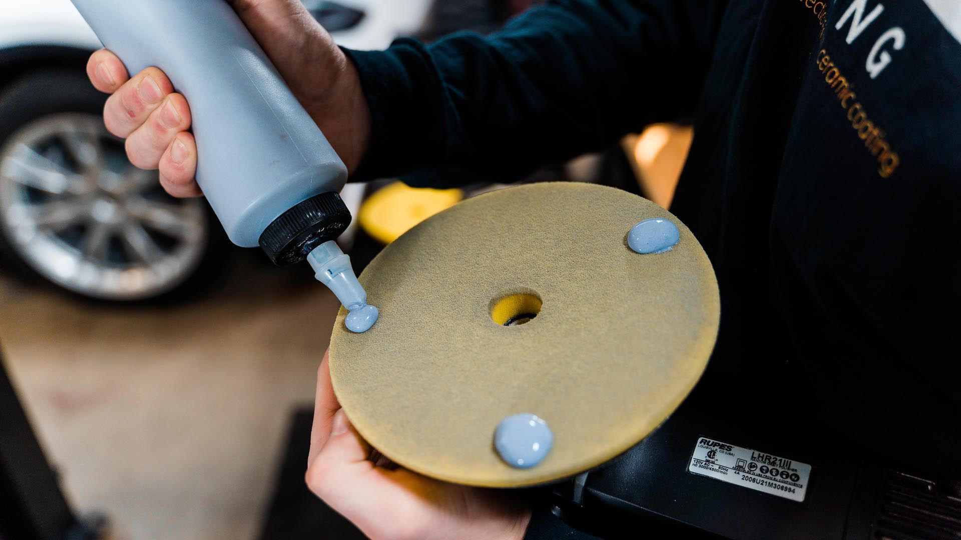 A person is holding a bottle of polish and a polishing pad.