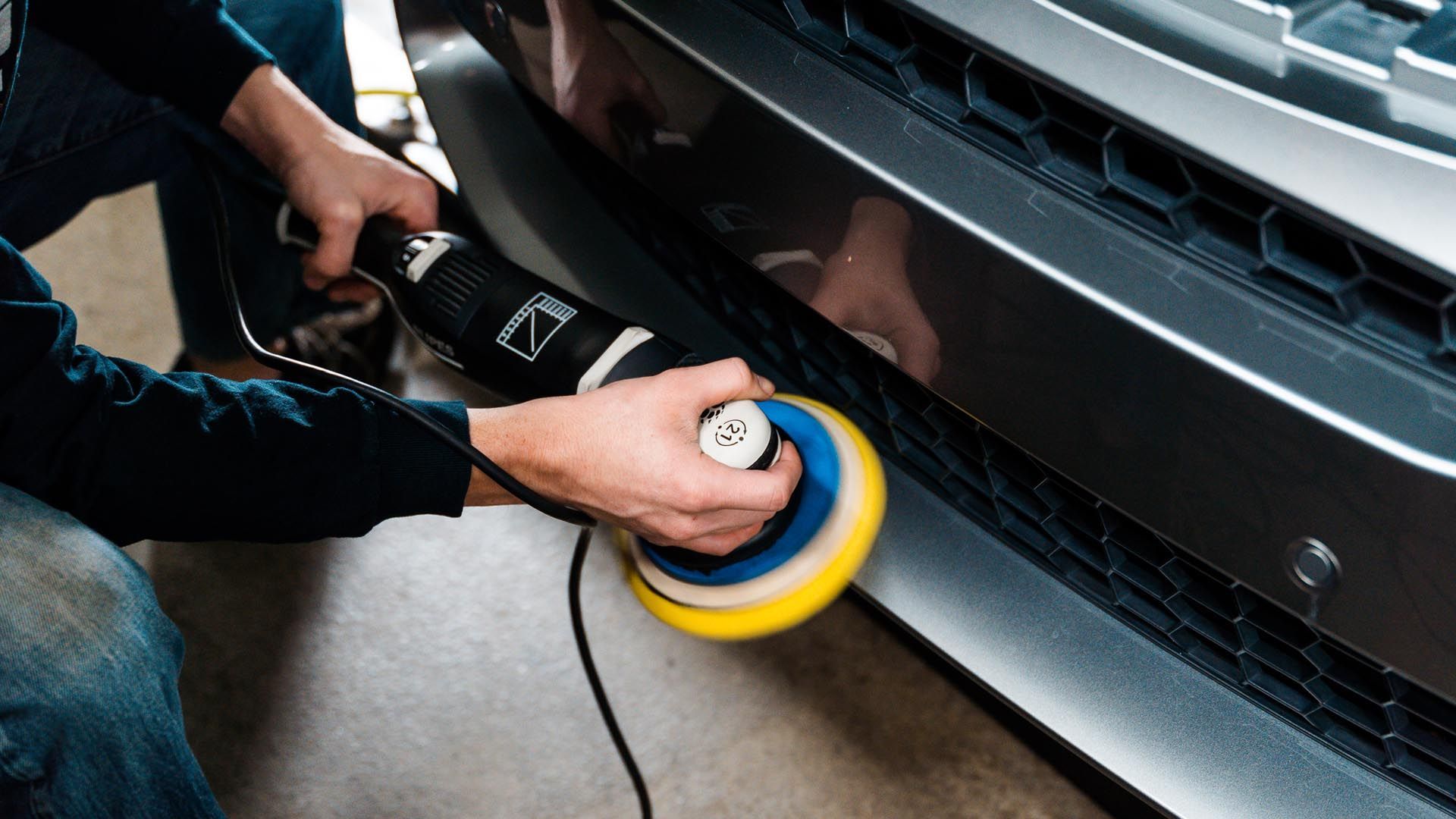 A man is polishing the bumper of a car with a machine.