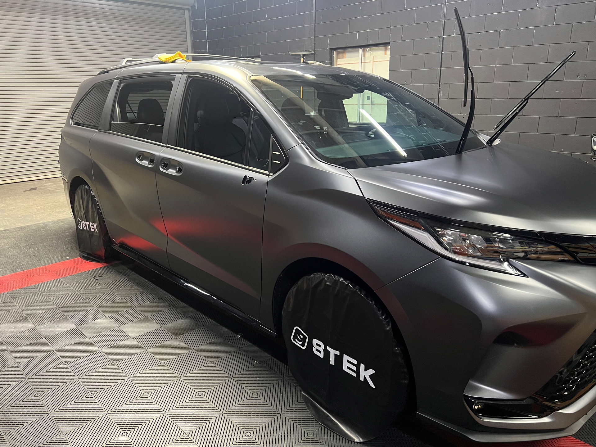 A gray car is parked in a garage with a tire cover that says btek on it.