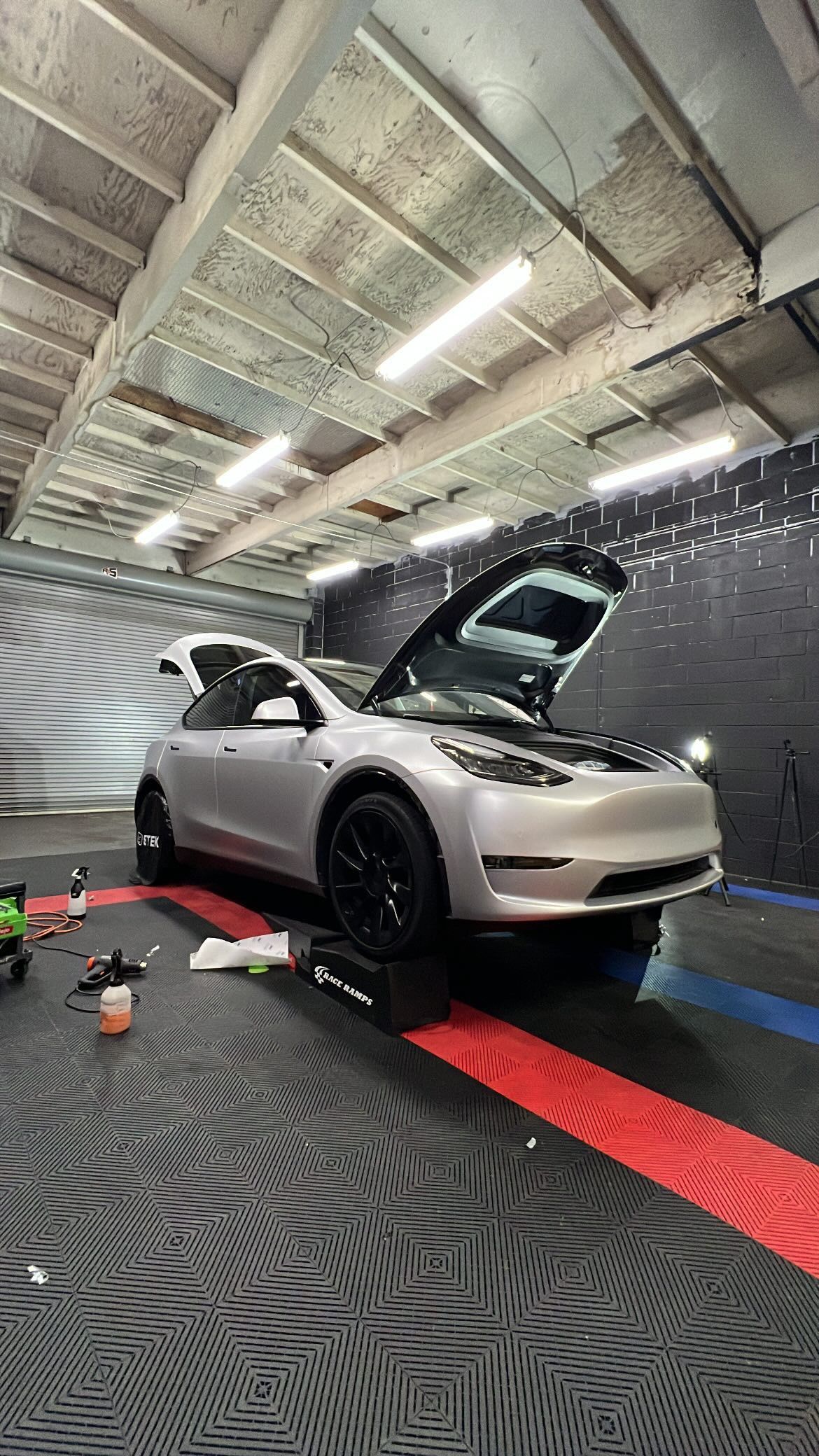 A tesla model 3 is parked in a garage with its hood up.