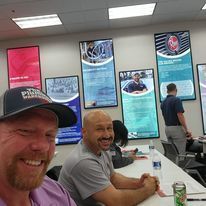 A man is sitting at a table in a room with a lot of pictures on the wall.