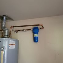 A water heater is hanging on a wall next to a pipe.