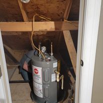 A water heater is sitting in the attic next to a door.