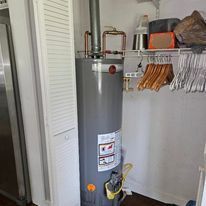 A water heater is sitting in a closet next to a refrigerator.