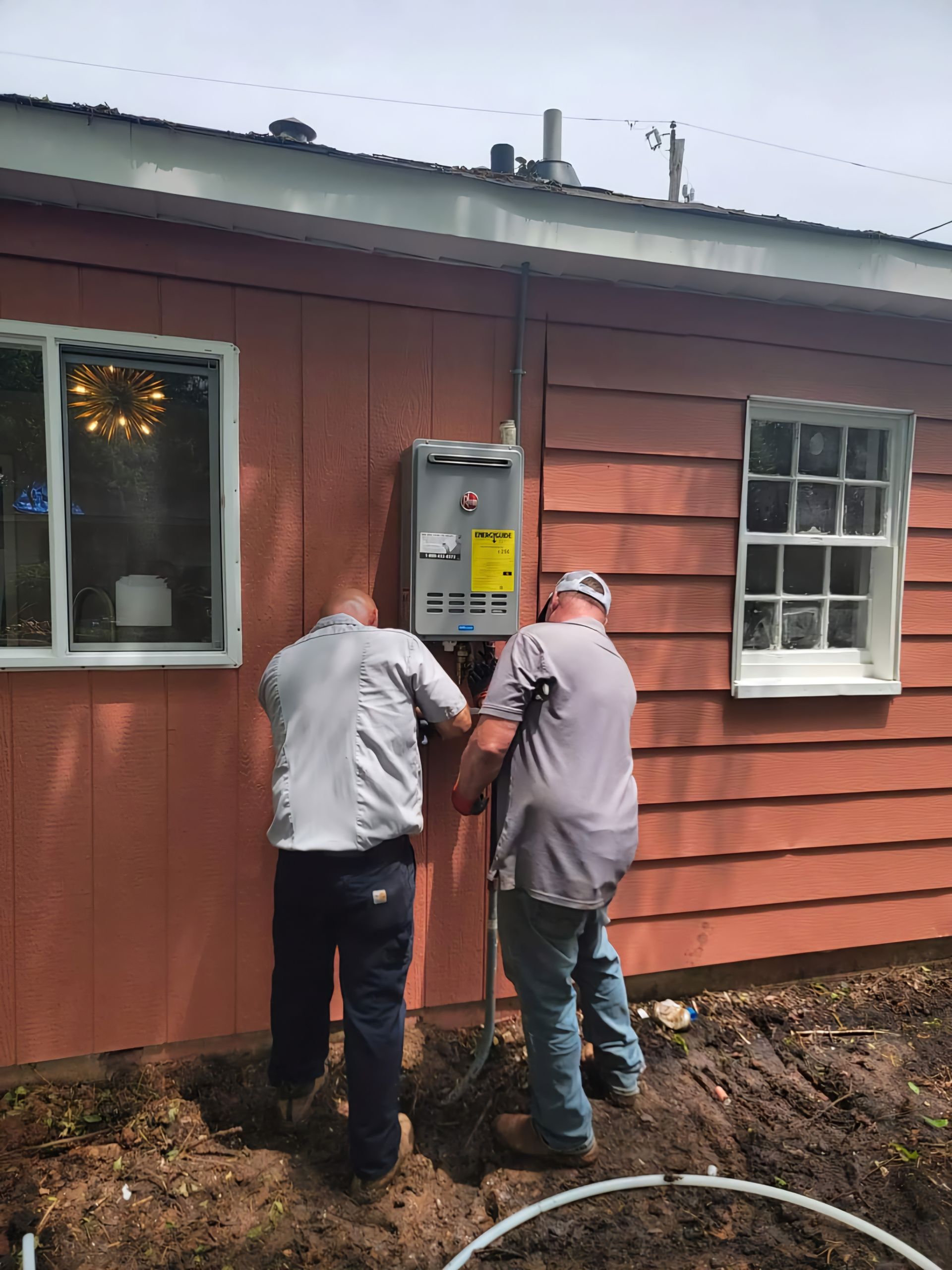 Two men are working on an electrical box on the side of a house.