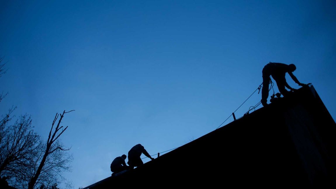 Silhouetted figures on a rooftop against a blue evening sky.