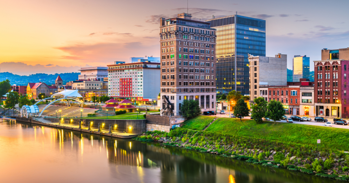 Skyline of Charleston, WV, with buildings along the Kanawha River at sunset.