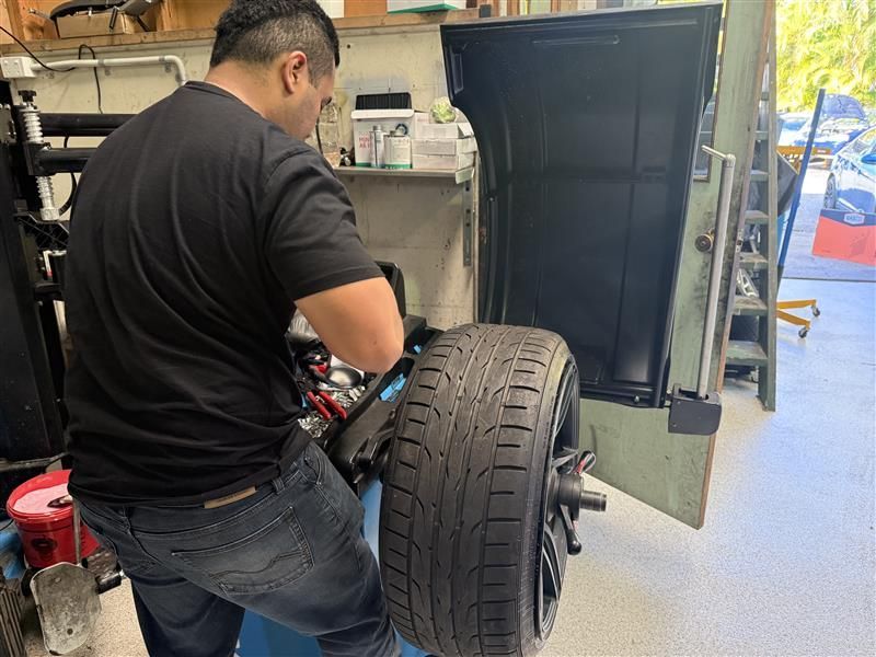 A Man In All Black Is Fitting A Tire To A Car — Automotive All Stars Car Service and Repair in Boronia Heights, QLD