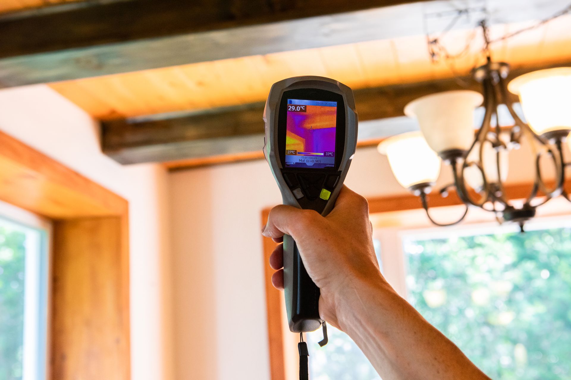 Person holding thermal camera pointed at wooden ceiling; interior shot.
