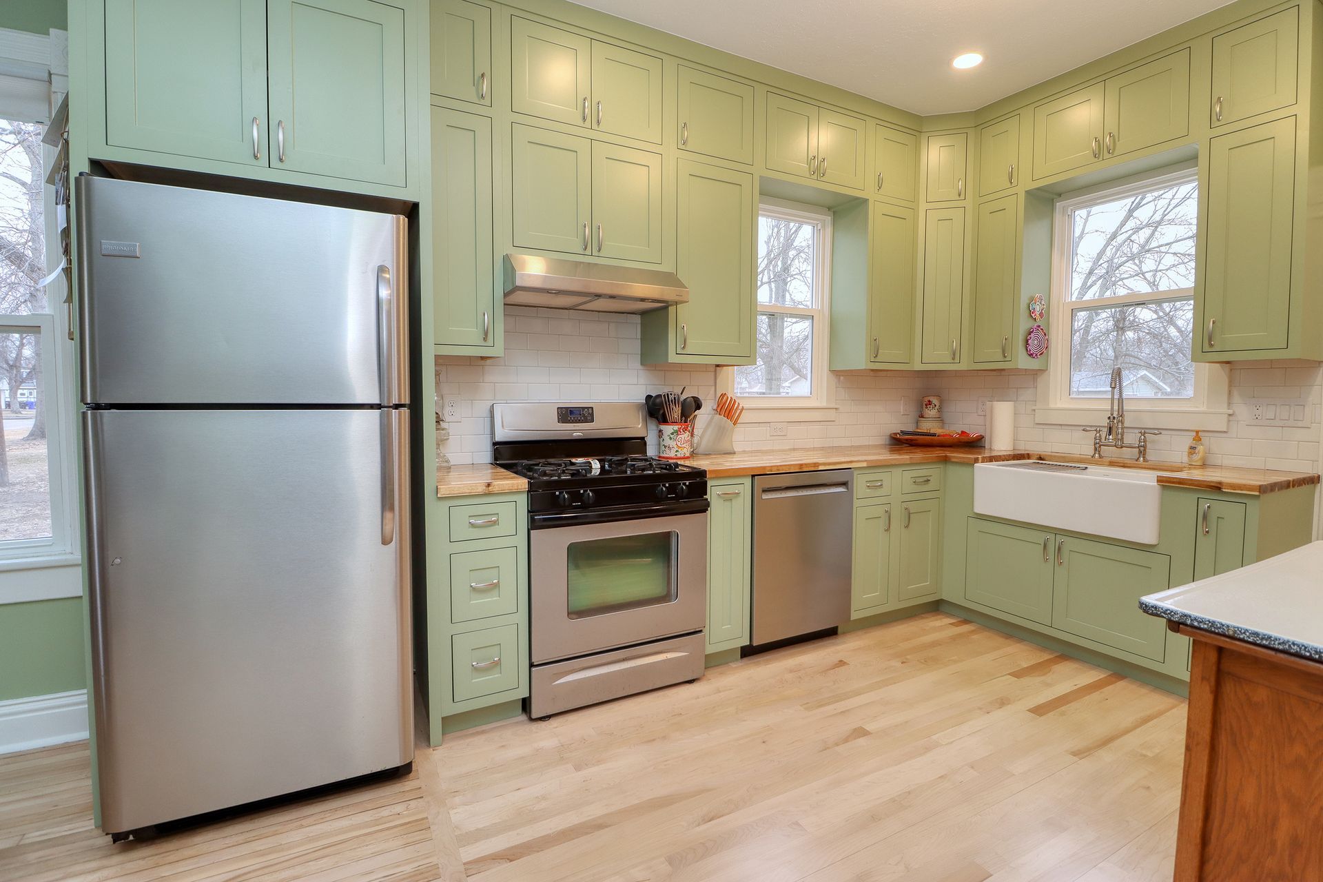 Kitchen with green cabinets, stainless steel appliances, and wood floors.