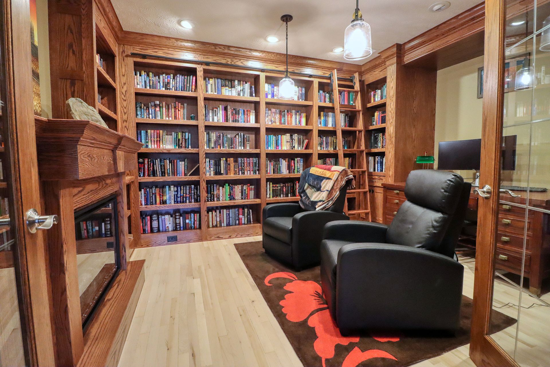 Cozy home library with built-in bookshelves, fireplace, two black chairs, and a ladder.