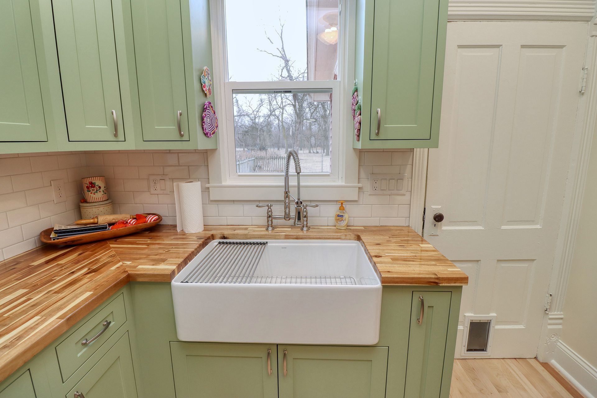 Kitchen with pale green cabinets, butcher block counters, and a white farmhouse sink.