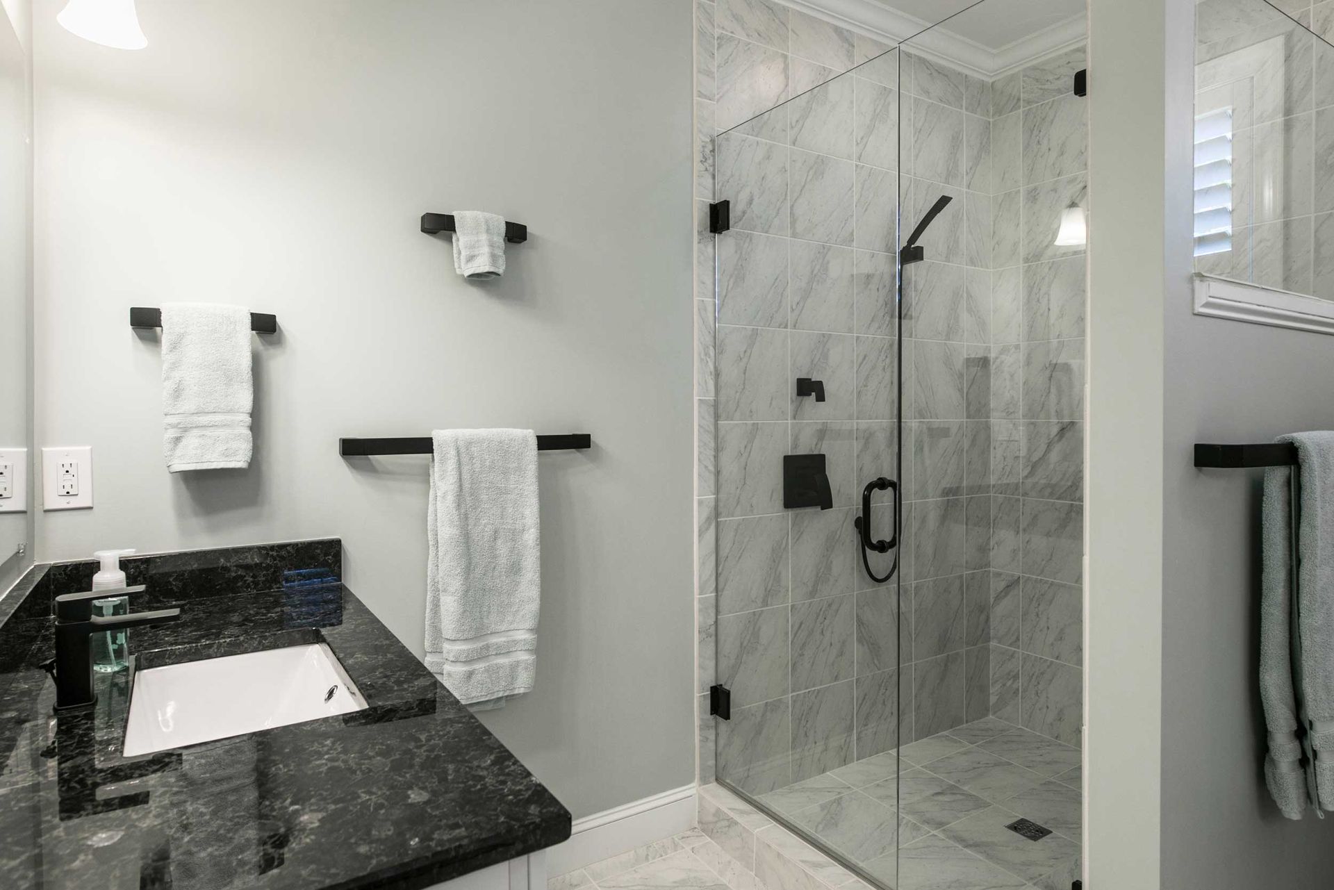 Modern bathroom with glass shower, marble tile walls, and vanity sink.