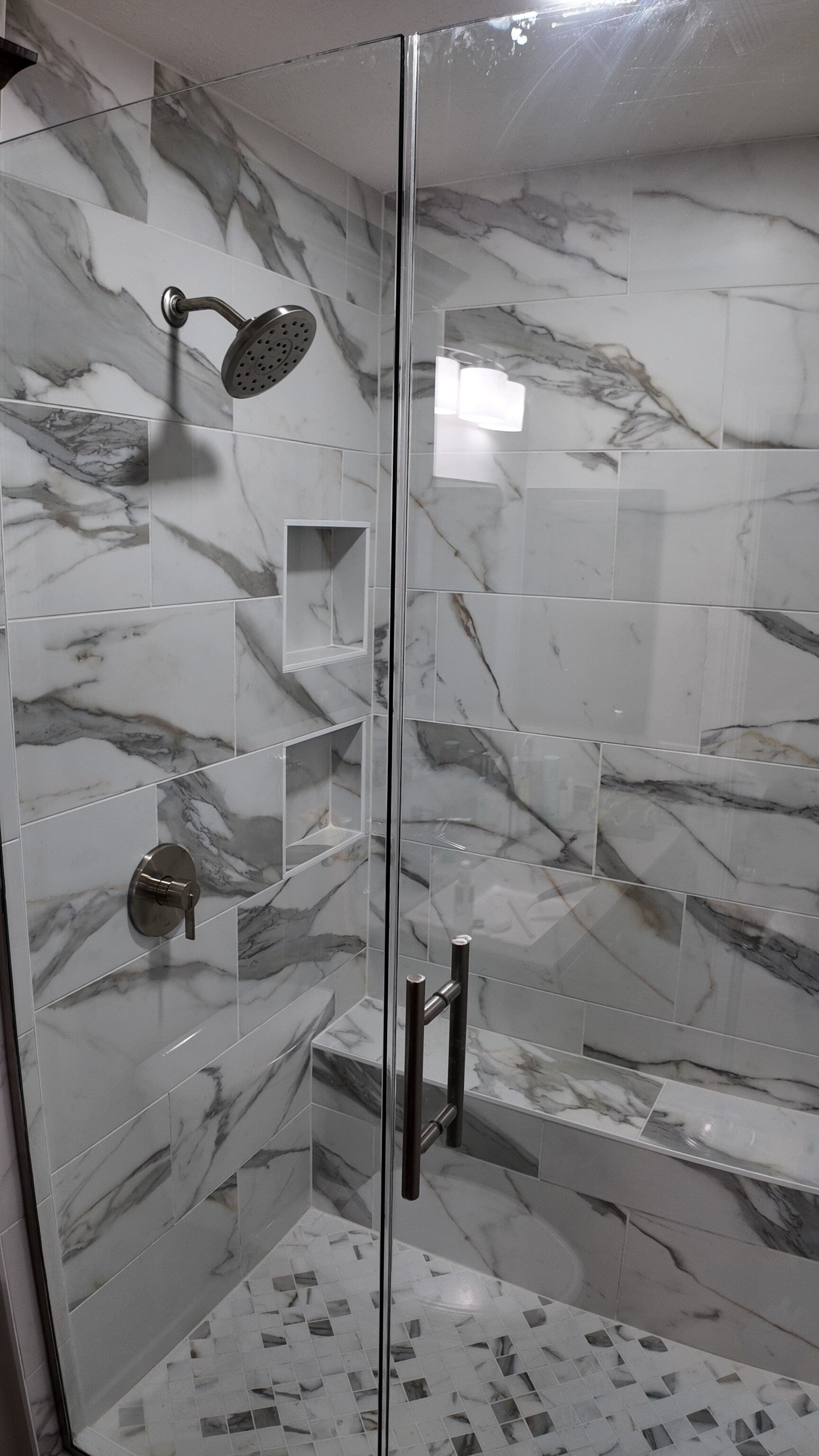 Shower with marble-look tile, glass door, and silver fixtures.