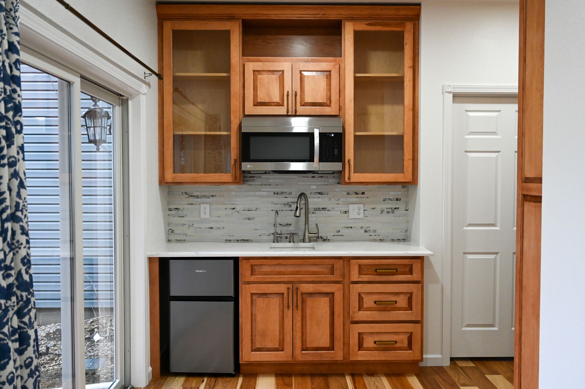 Small kitchenette with light wood cabinets, microwave, sink, and mini-fridge.