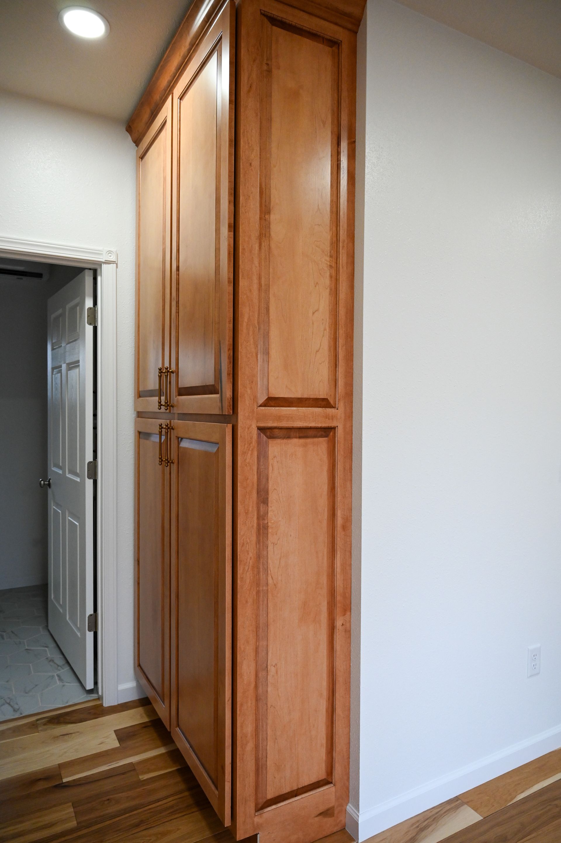 Tall, light brown wooden cabinet against a white wall and near a doorway.