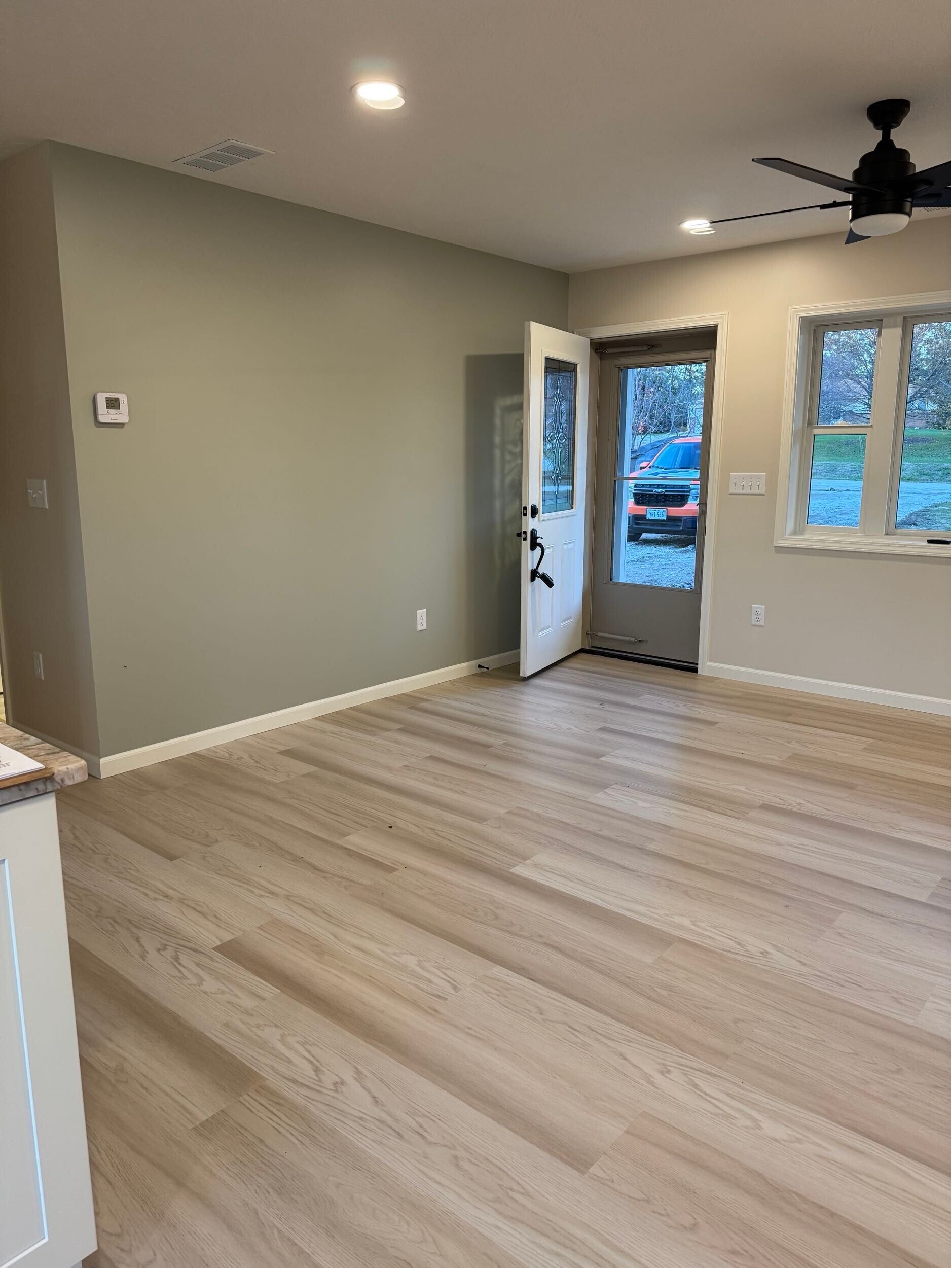 Empty living room with light wood floors, neutral walls, and an open door.