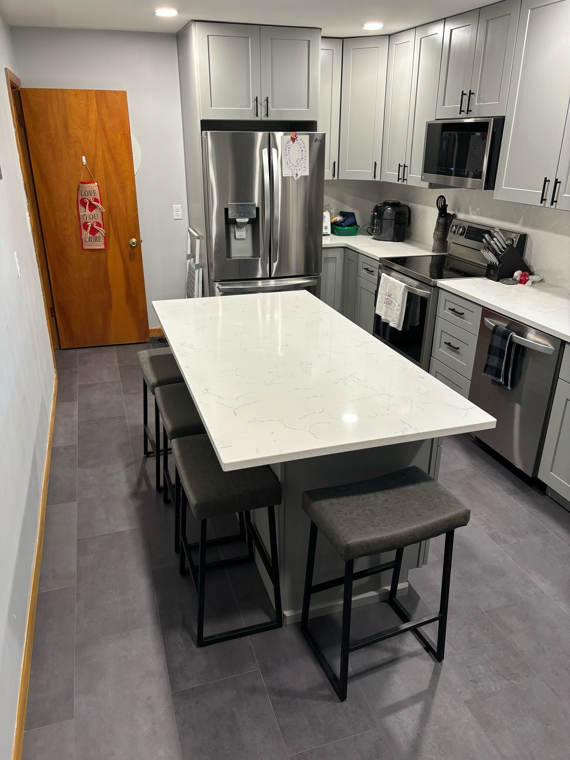 Modern kitchen with gray cabinets, island with stools, stainless steel appliances, and wood door.