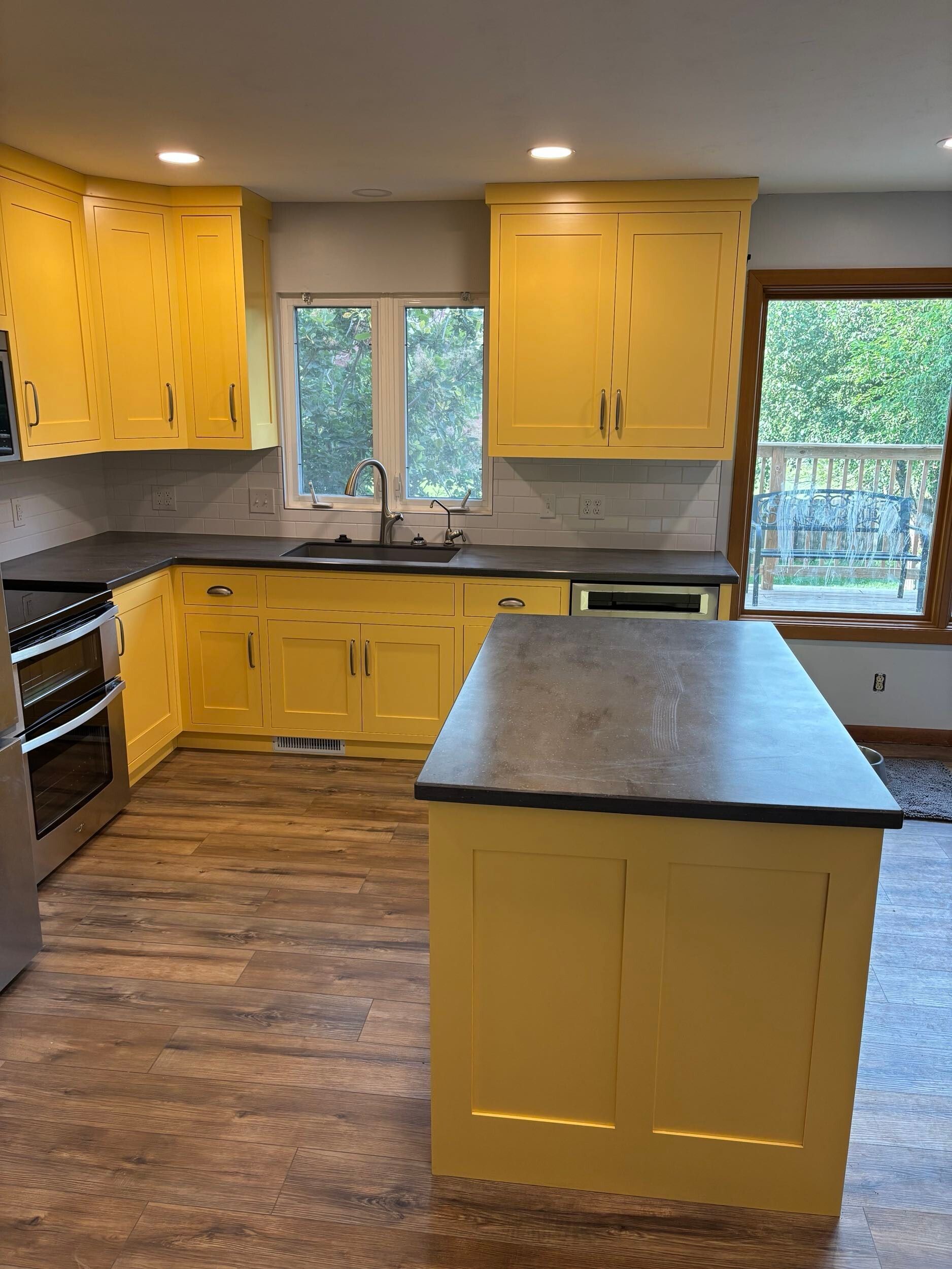 Yellow kitchen cabinets with gray countertops and island, wooden floor.