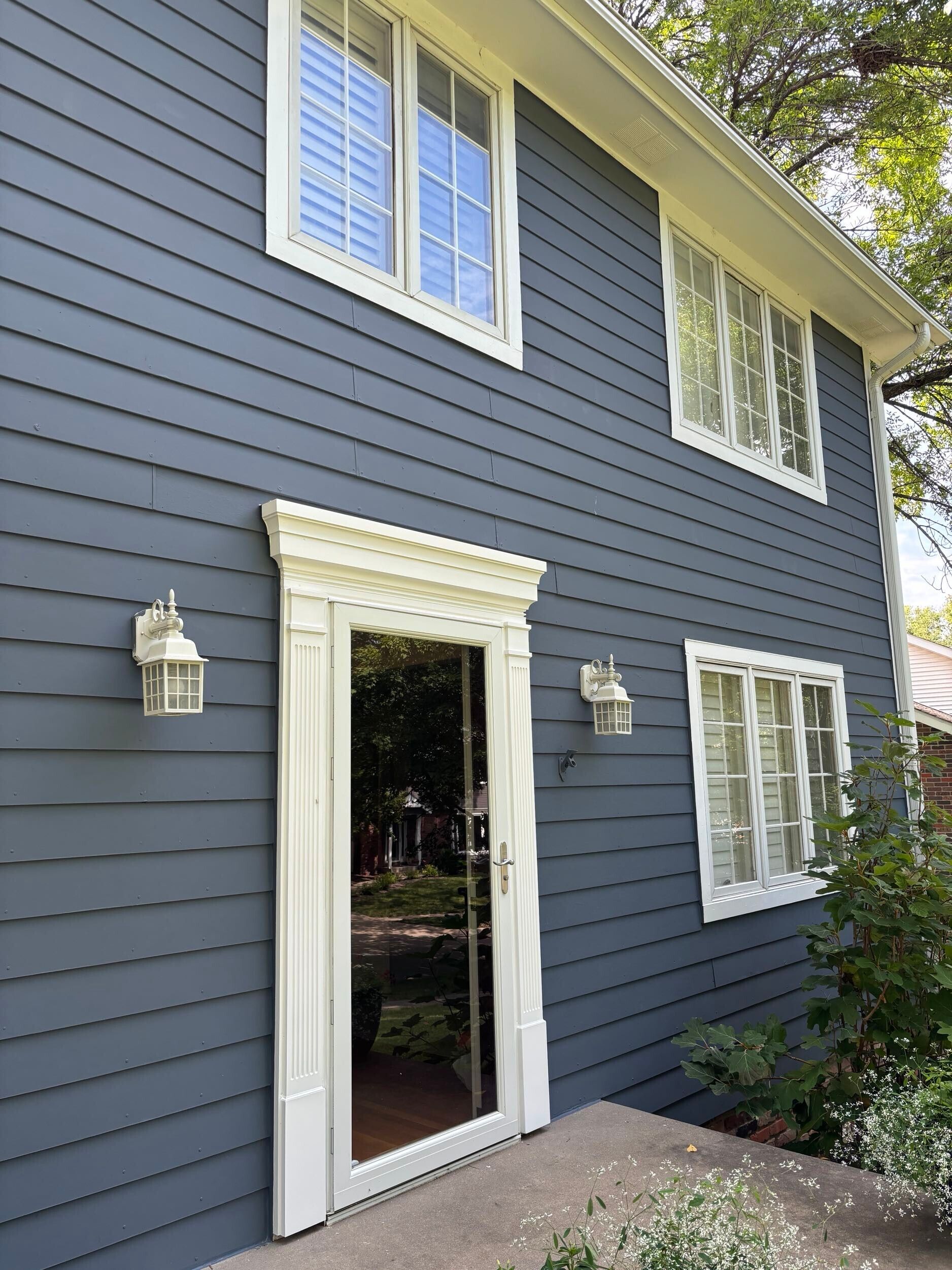 Blue house with white trim, windows, and entry door. Two-story building, bright natural lighting.