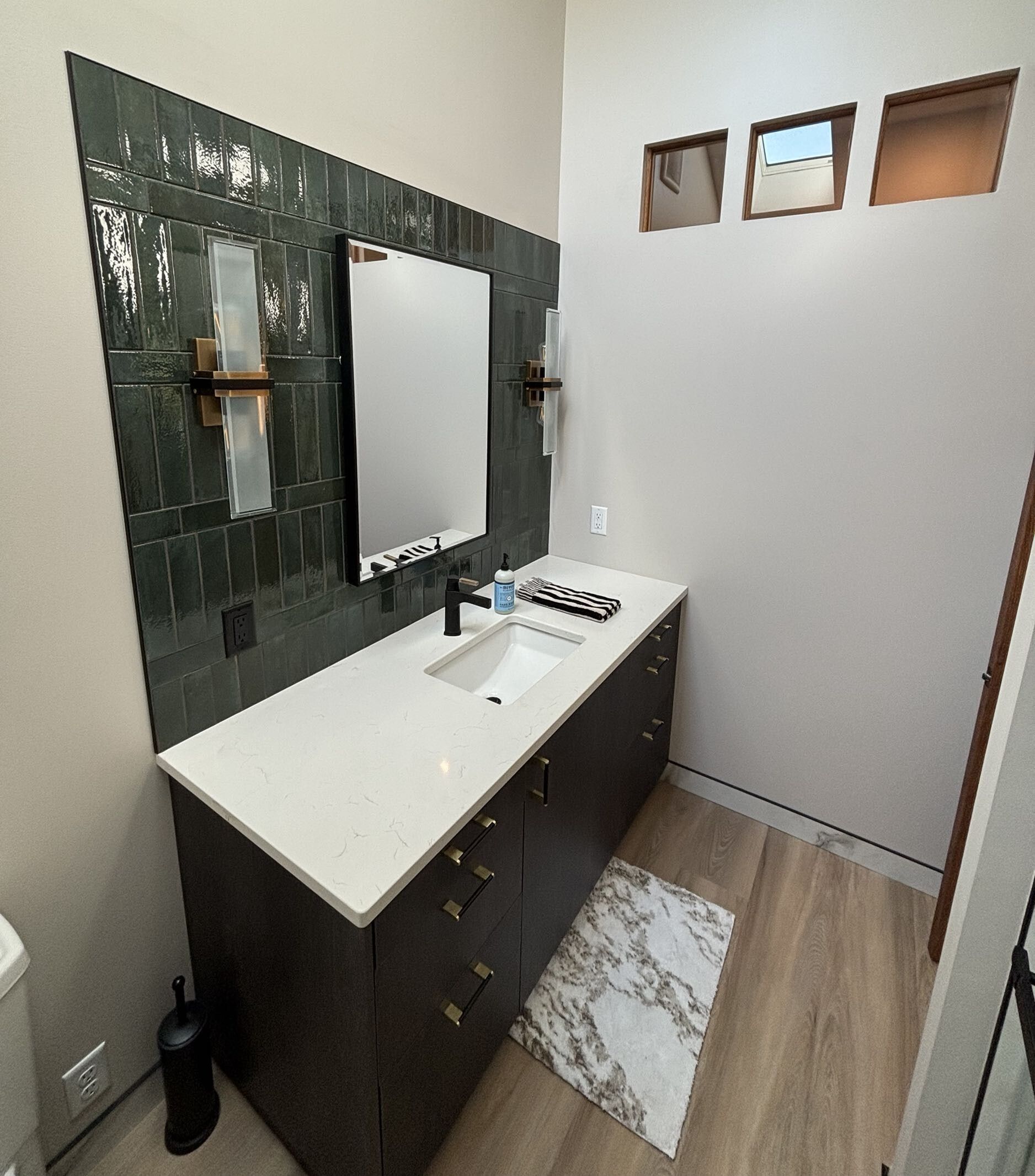 Bathroom with dark cabinetry, white countertop, green tile accent wall, and mirror.