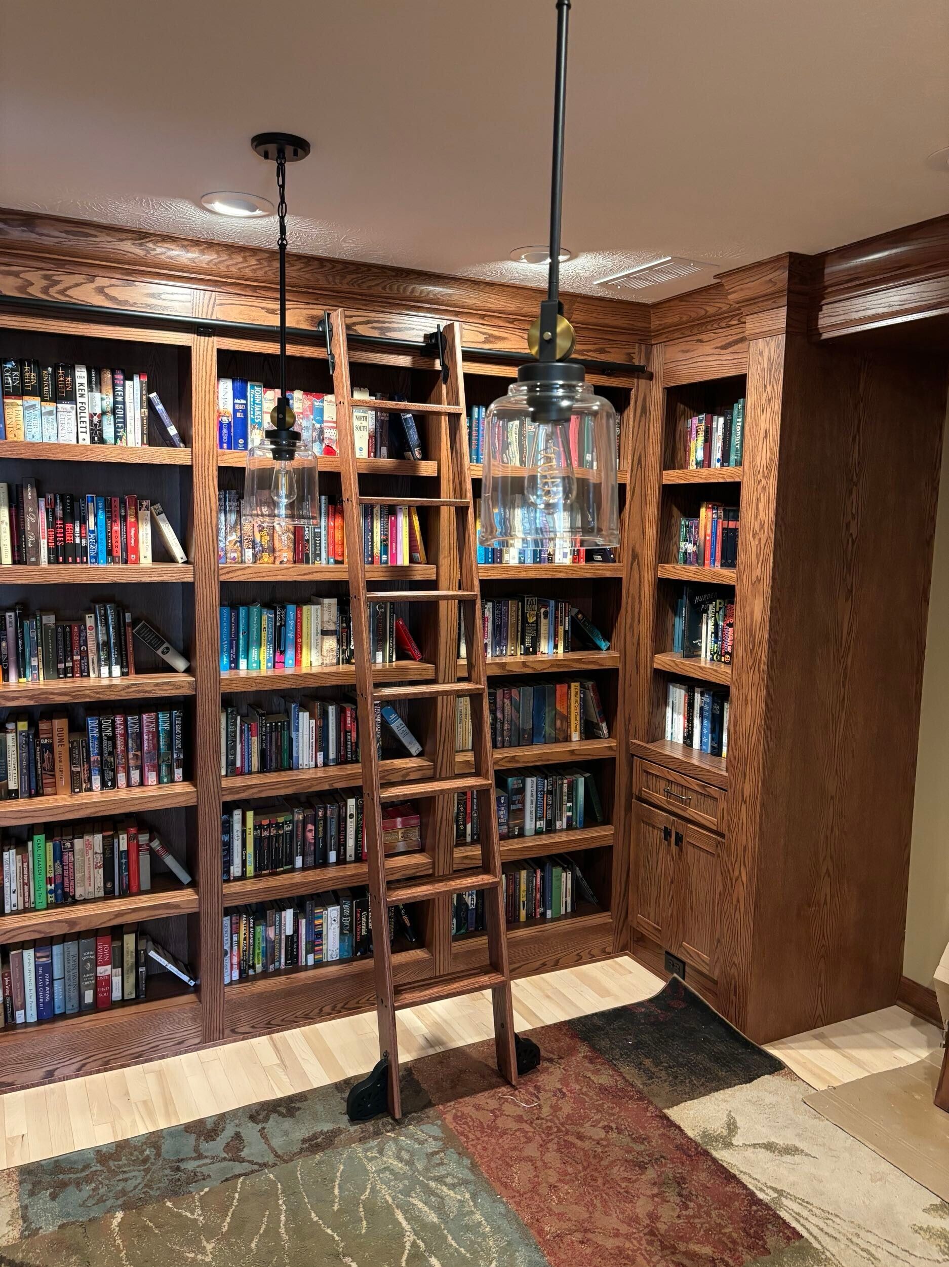Wooden bookshelves filled with books, a rolling library ladder, and two pendant lights.