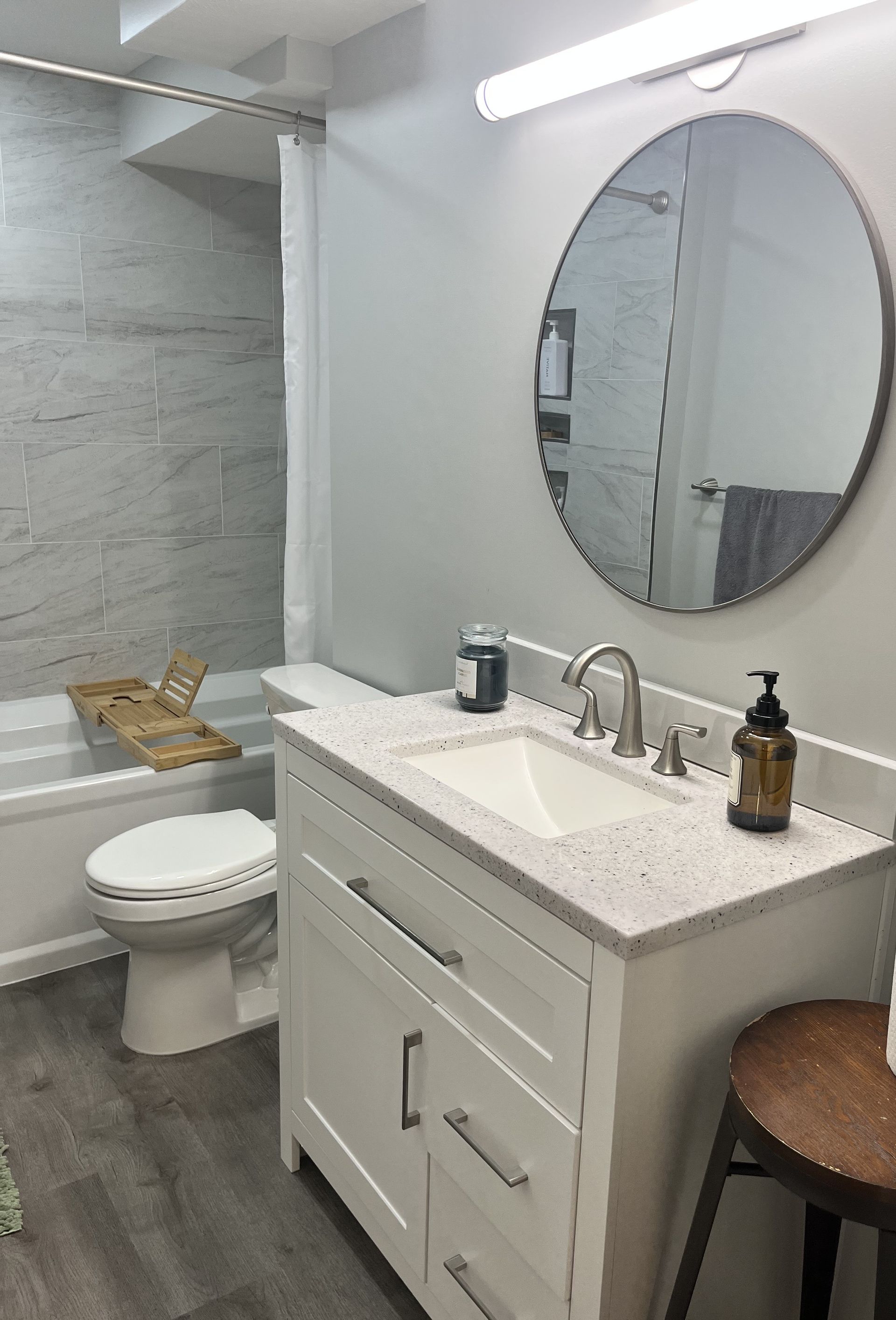 Bathroom with white vanity, round mirror, gray walls, and a tub/shower combination.